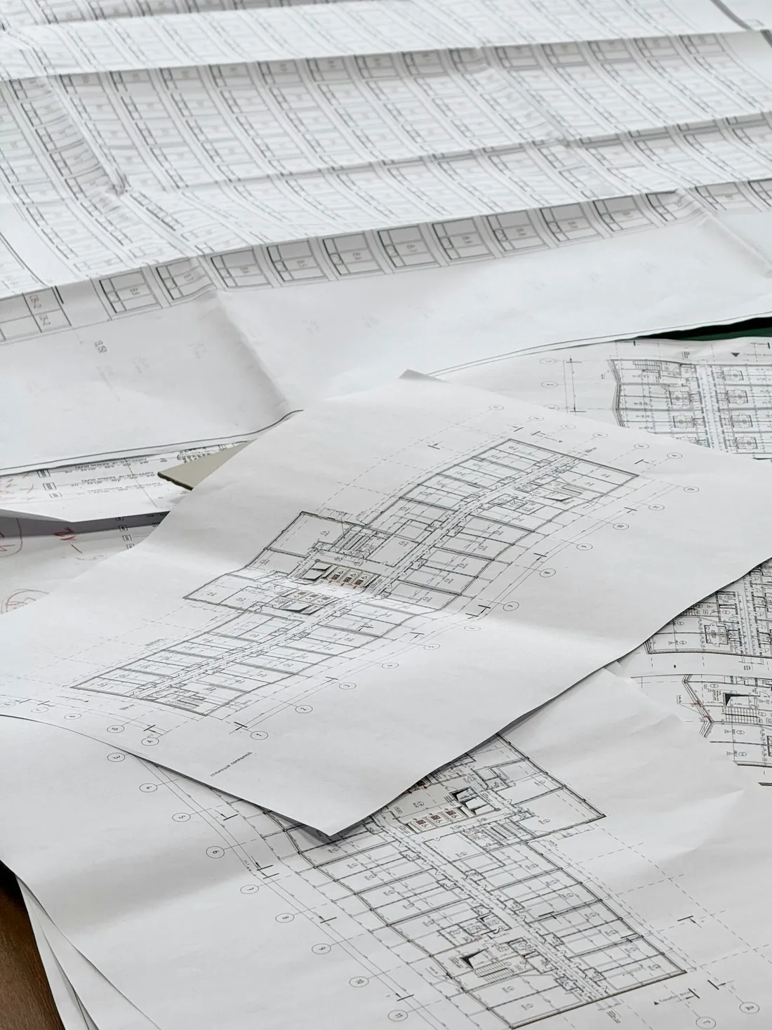 Architectural drawings spread across a desk, sheets of plans overlapping