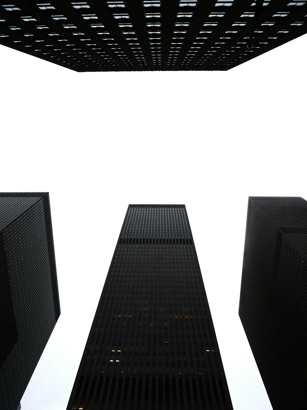 Three dark skyscrapers seen from below against a white sky